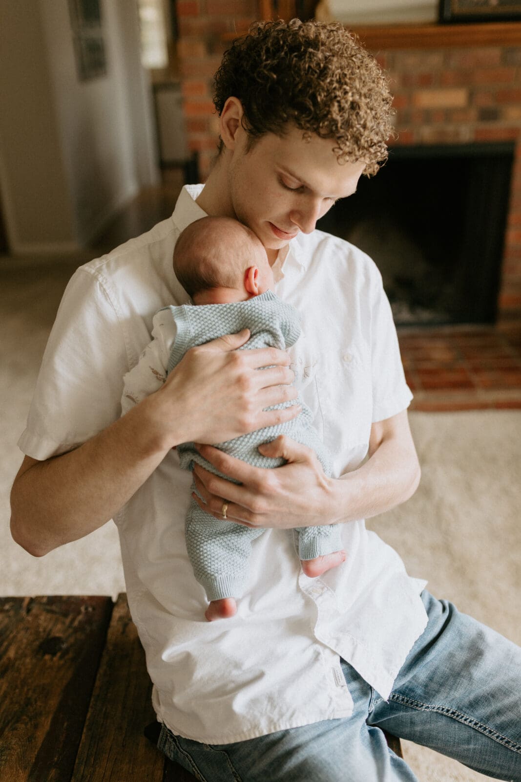 A new dad holds his newborn baby to his chest and looks down at him for this West Lafayette, Indiana lifestyle newborn photography session.