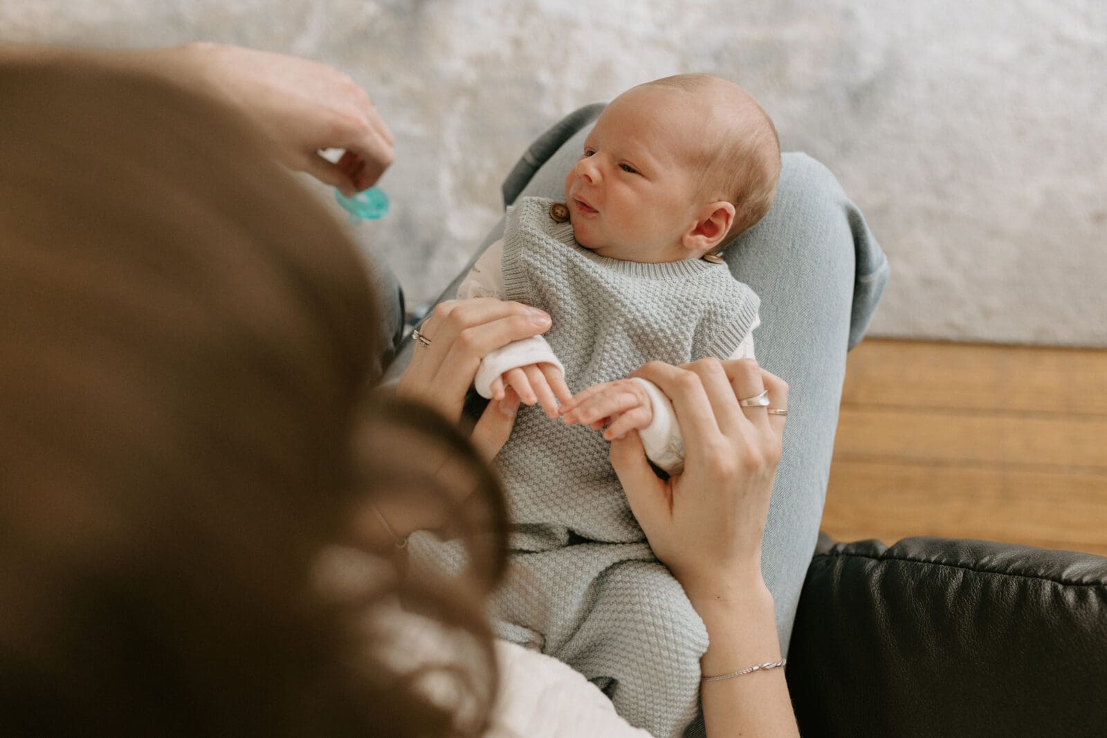 A camera view from above of a newborn baby resting on the legs of his mother. He looks like he is about to cry. A pacifier is about to be offered to the baby.