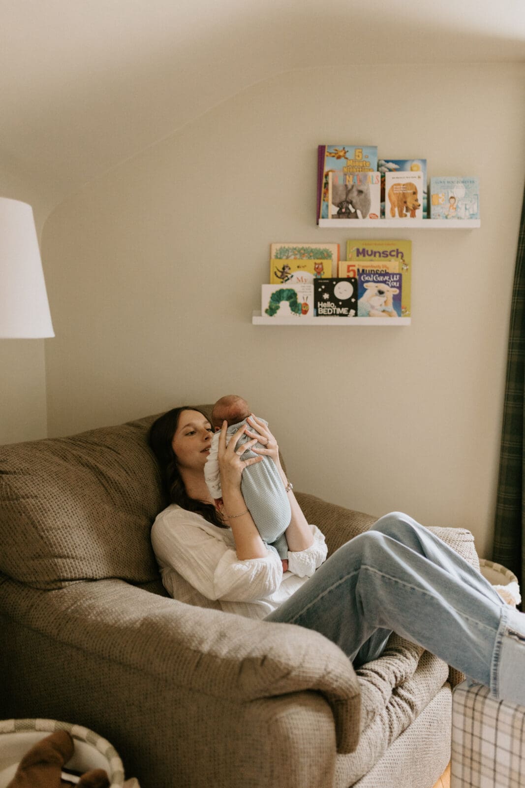 A new mom holds her newborn baby boy close to her face and smiles at him while sitting in an oversized recliner.
