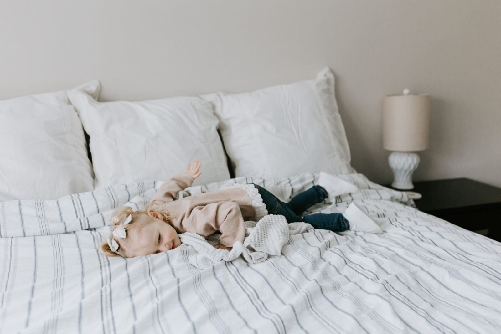 A toddler lays on the bed and smiles.