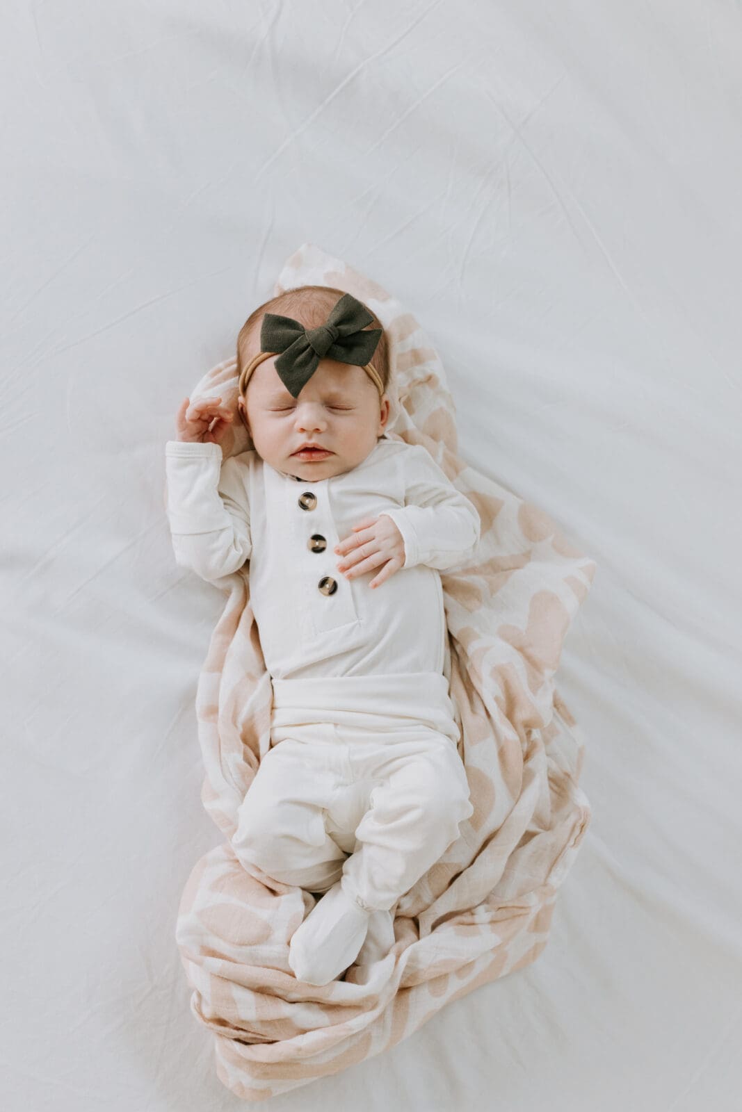 A photo taken from above of a newborn baby sleeping on a white sheet, nestled in a pink swaddle blanket. Lifestyle newborn photo shoot in Lafayette, Indiana.