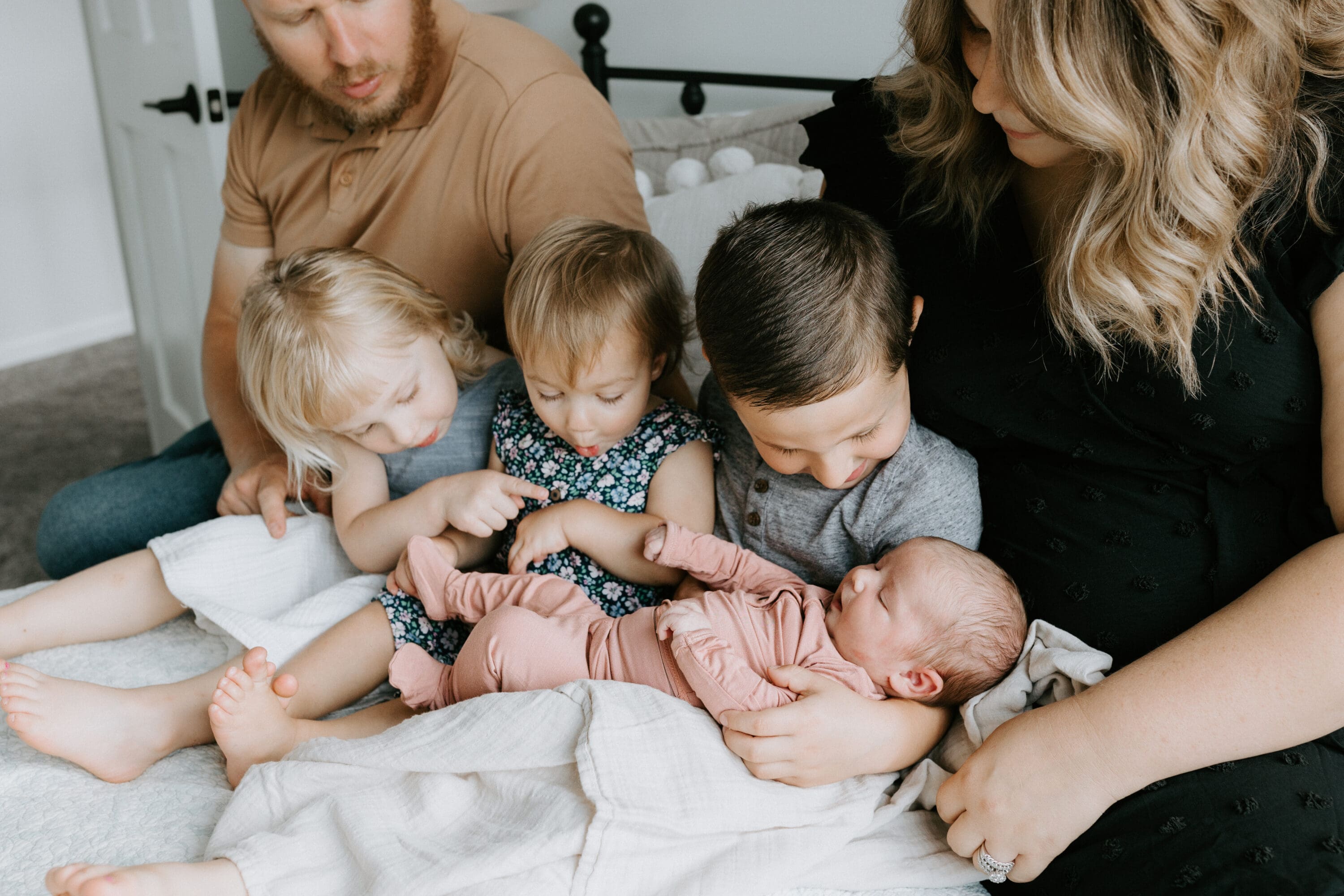 A mom and dad sit on a bed with three children and newborn baby between them. 