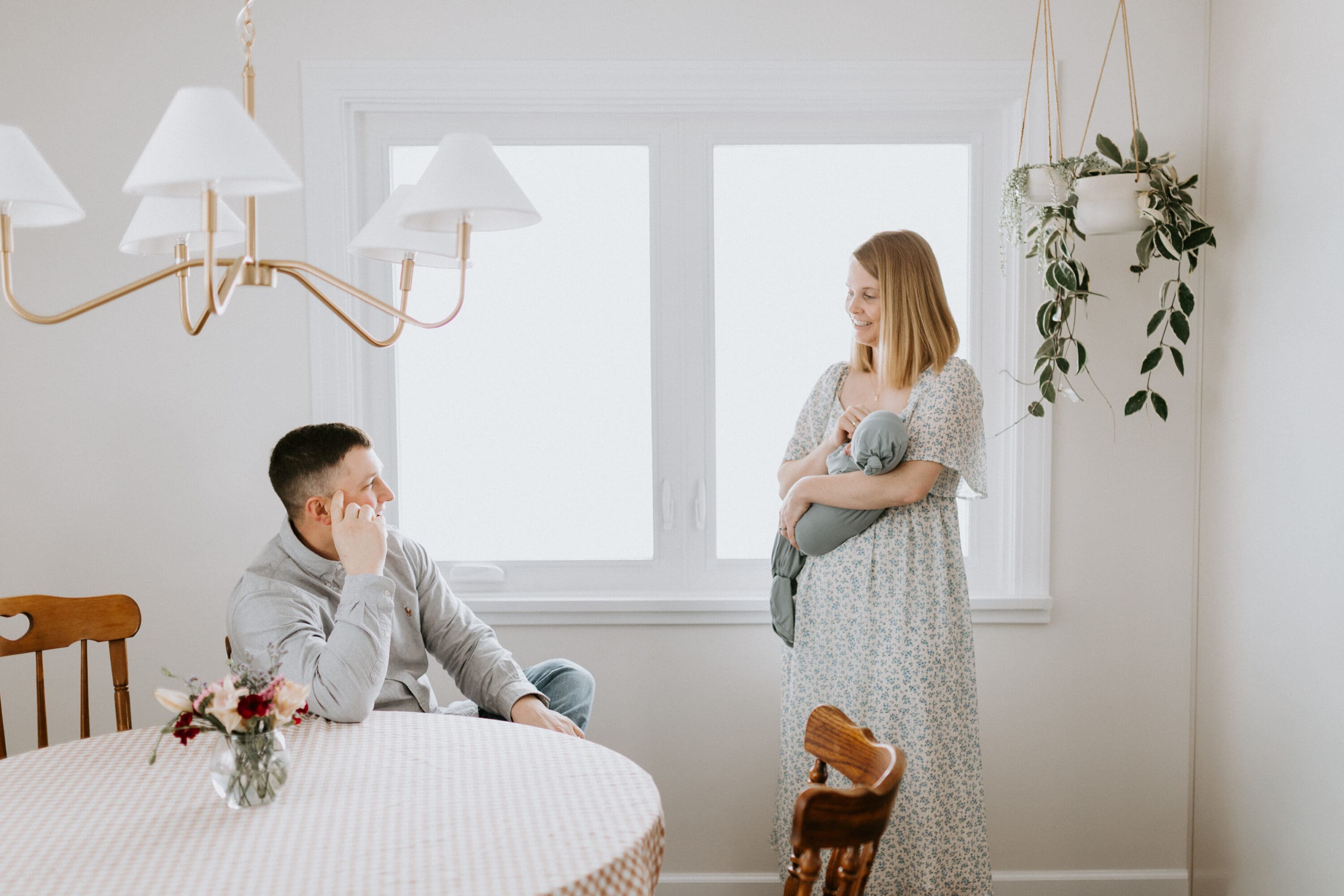 A new mom holds her baby while talking to her husband who sits next to her on a chair.