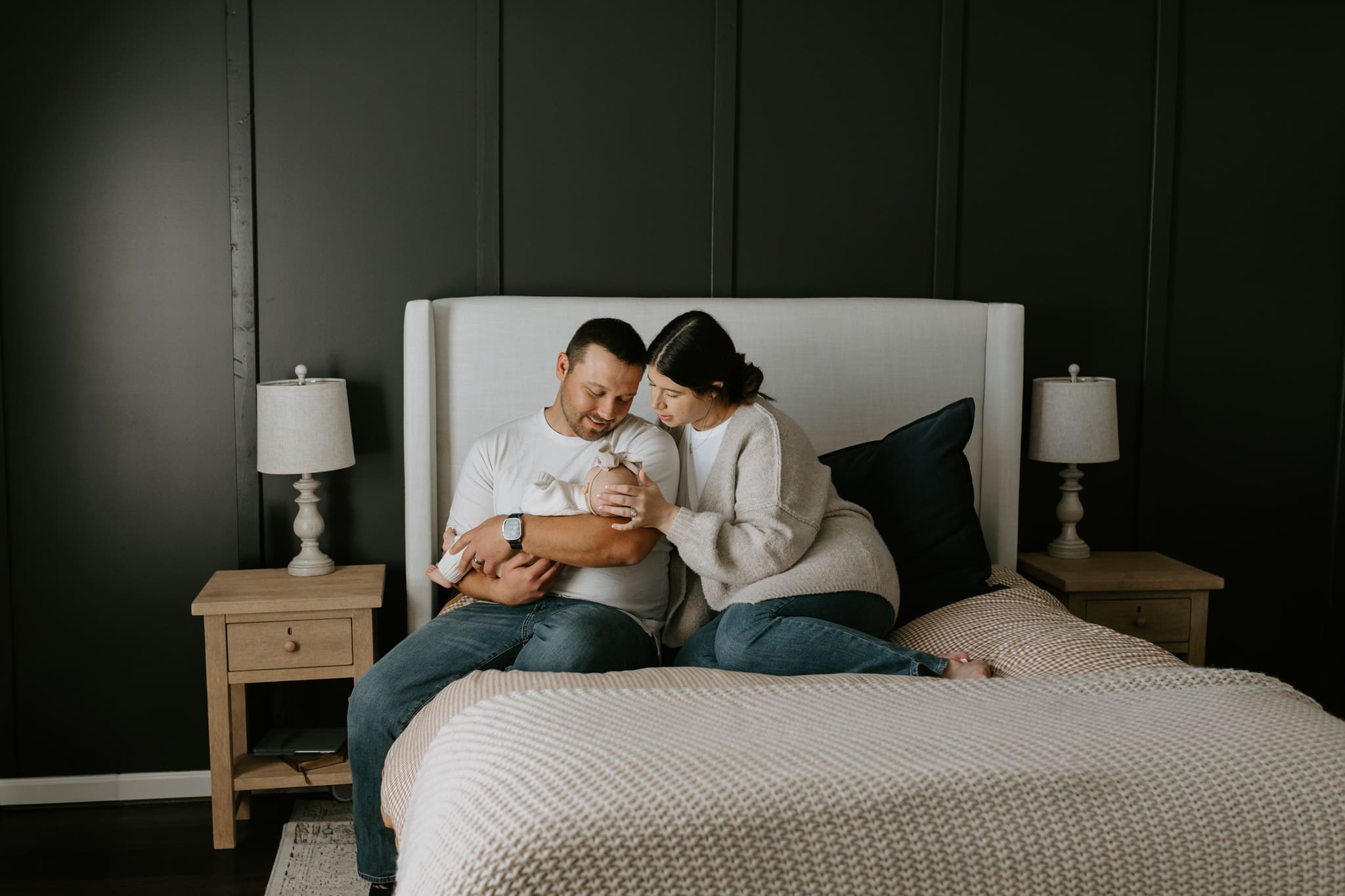 A couple sits on the bed holding their newborn daughter.