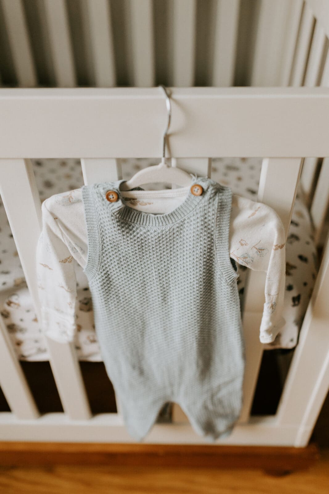 A knit newborn baby outfit hangs on the edge of a white baby crib.