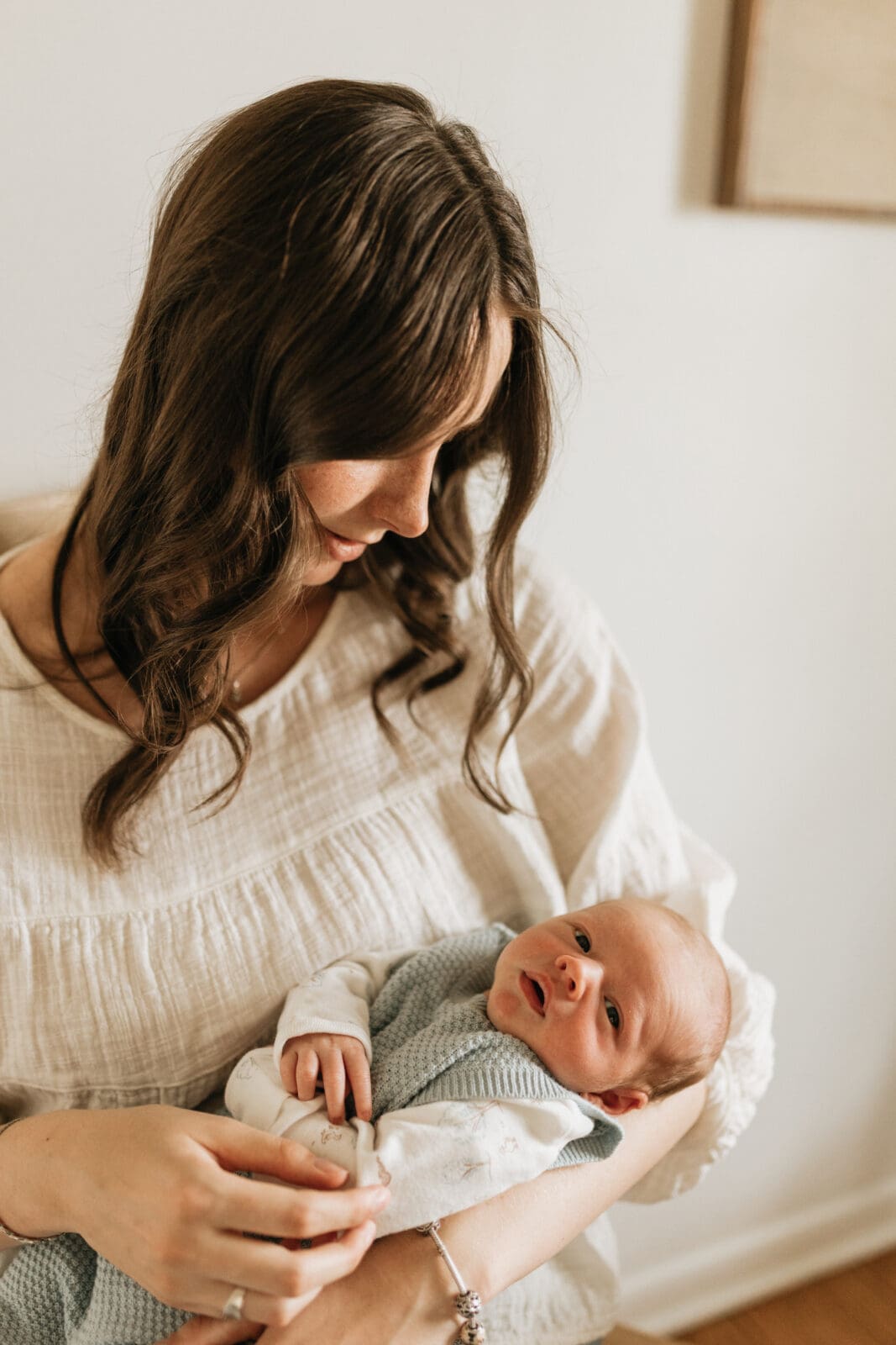 A close up photo of a mom looking down at her newborn baby while the baby looks up into the camera.