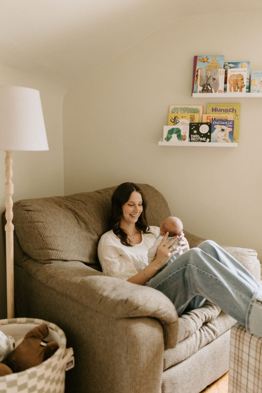 A new mom smiles widely at her newborn baby son as she sits in an oversized chair in the baby's nursery.