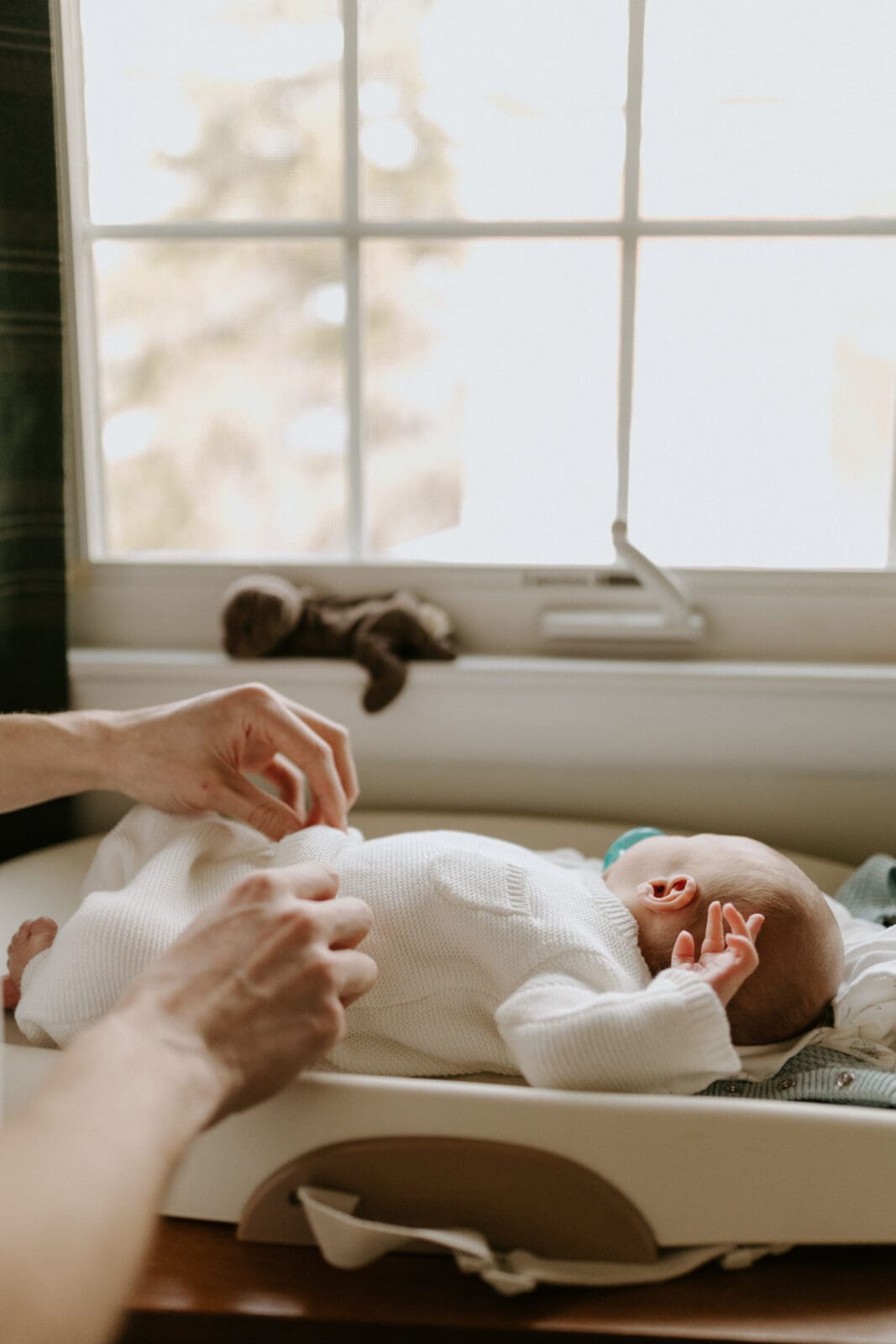 A lifestyle newborn photo by Vanessa Stoller photography of a baby laying on a changing table under a large window.
