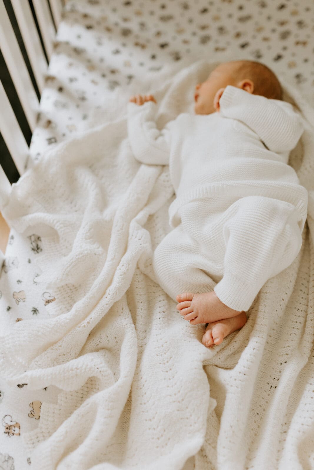 A baby sleeps in his crib. The focus of the image is on the baby's feet and toes.