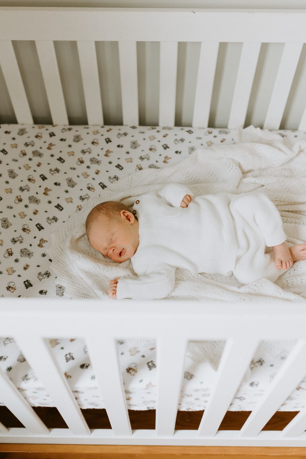 A baby sleeps in his crib. The angle of the photo is looking over the edge of the white crib.