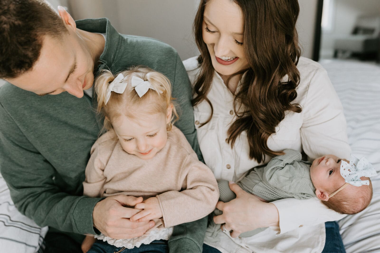 A close up photo of a family of four interacts with smiles and snuggles.