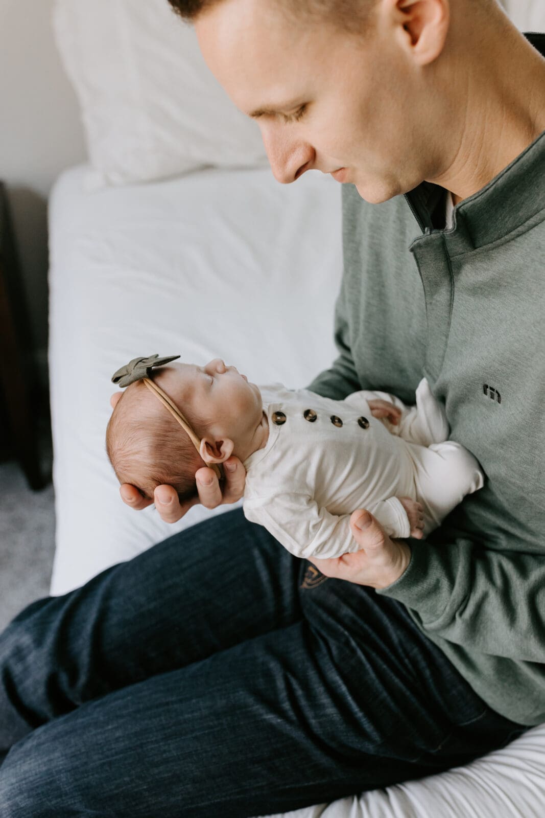 A dad holds his sleeping newborn daughter in his hands and peacefully and lovingly gazes down at her.