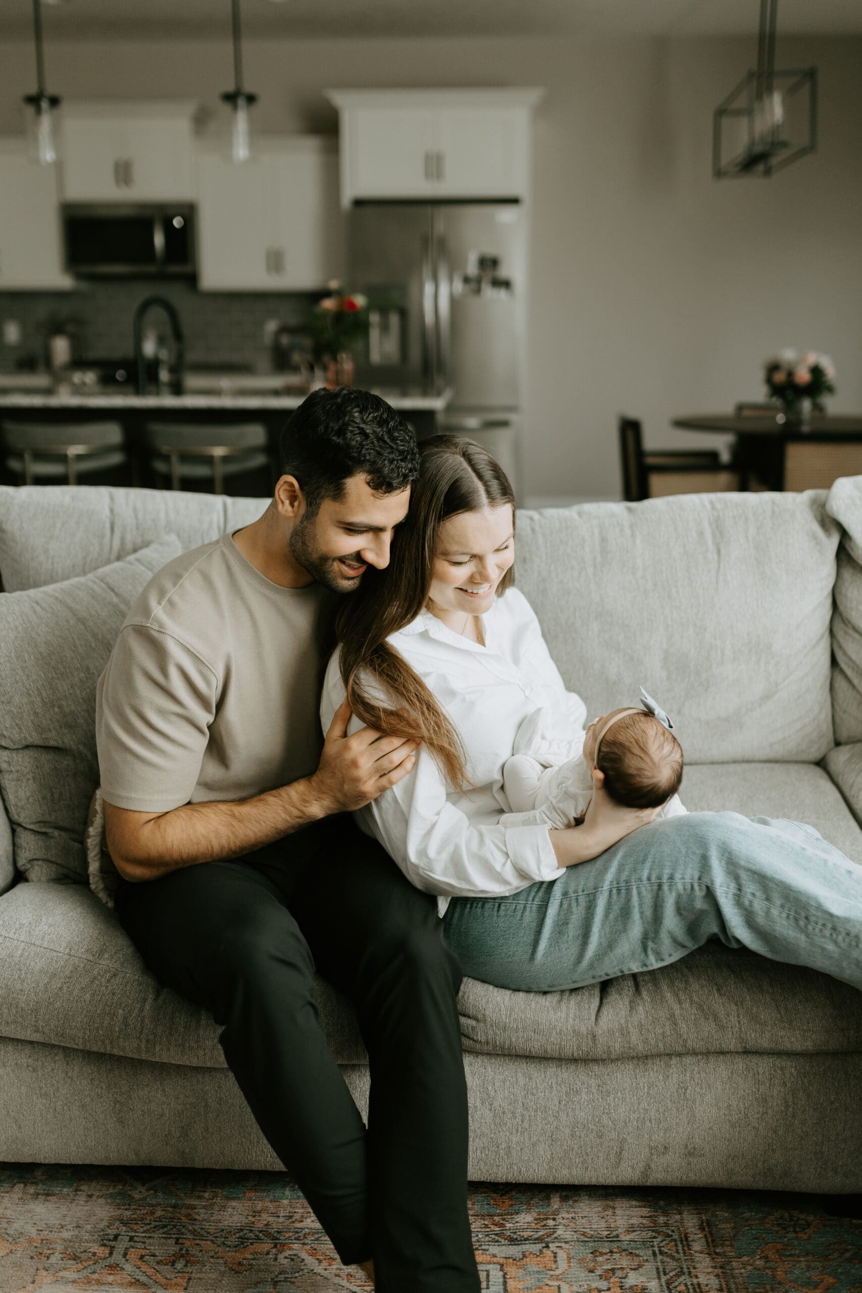 A husband and wife sit with their baby on the sofa for their newborn session in Lafayette, Indiana.