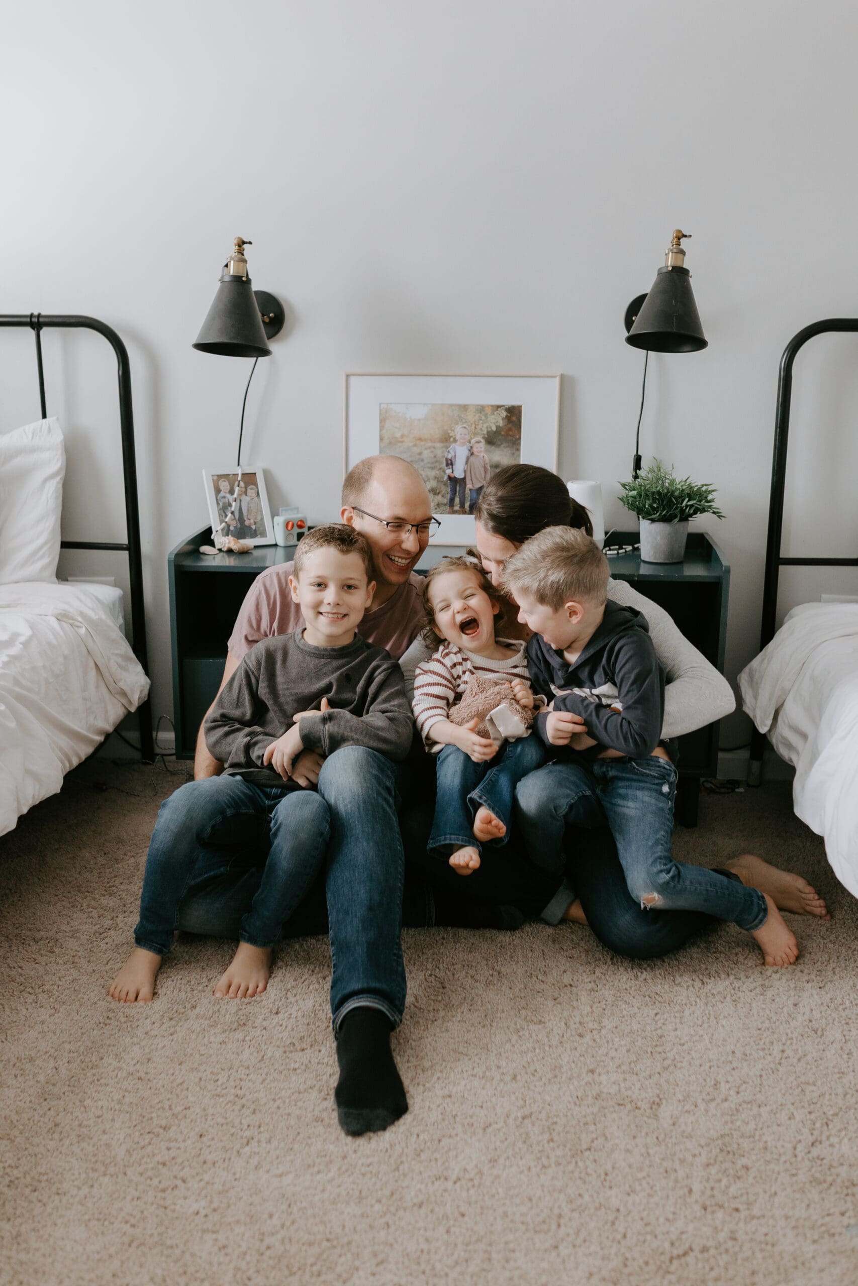 A family sits on the floor of a kids bedroom laughing and cuddling together.