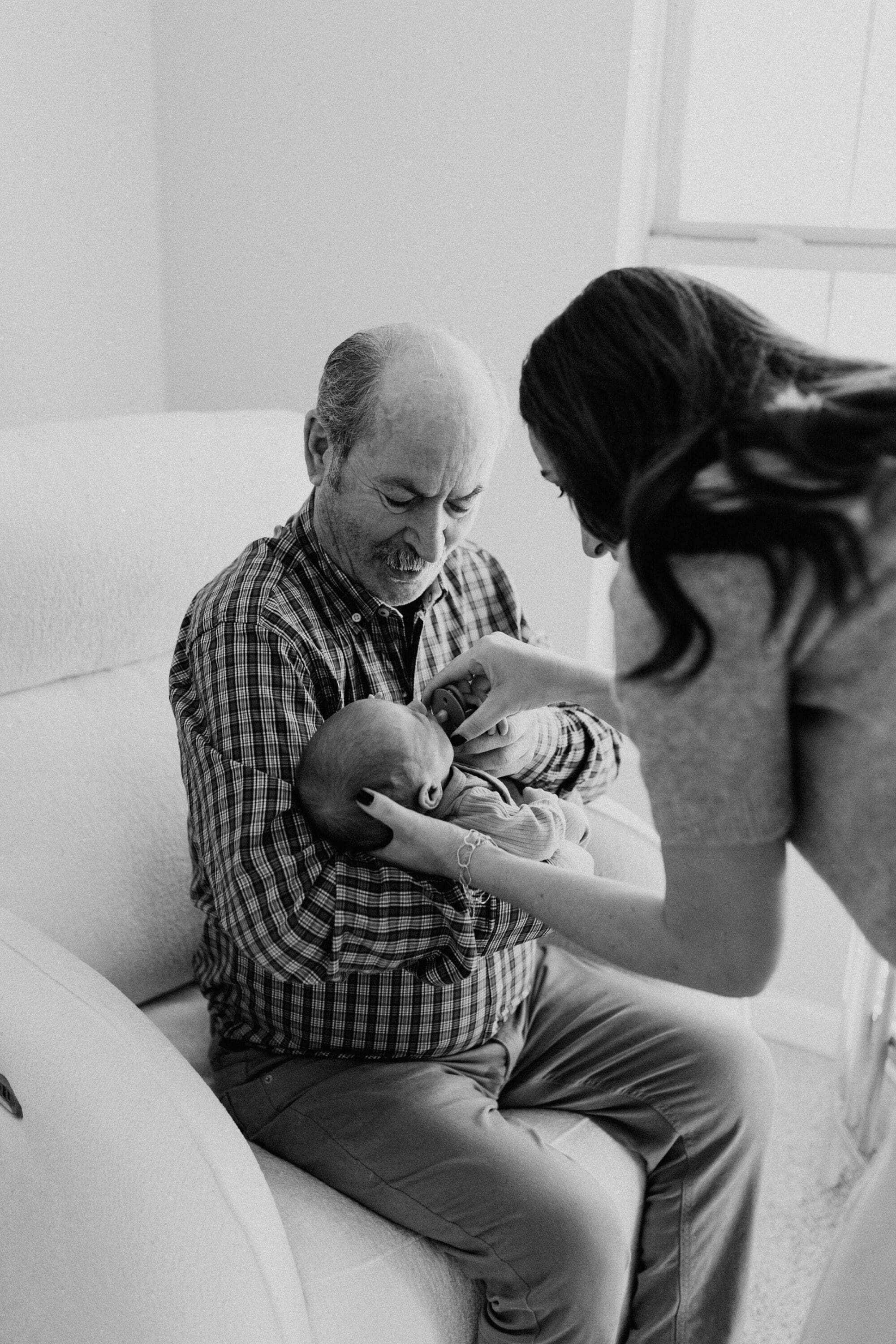 A new mom is placing a newborn baby into the arms of his grandfather during a newborn session in Lafayette, Indiana.