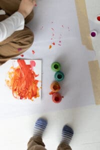 children's paint bottles beside an orange and red painting