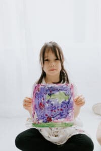 a girl holds a purple painting in a white studio