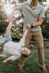 A small child is laughing while being playfully swung by his dad.