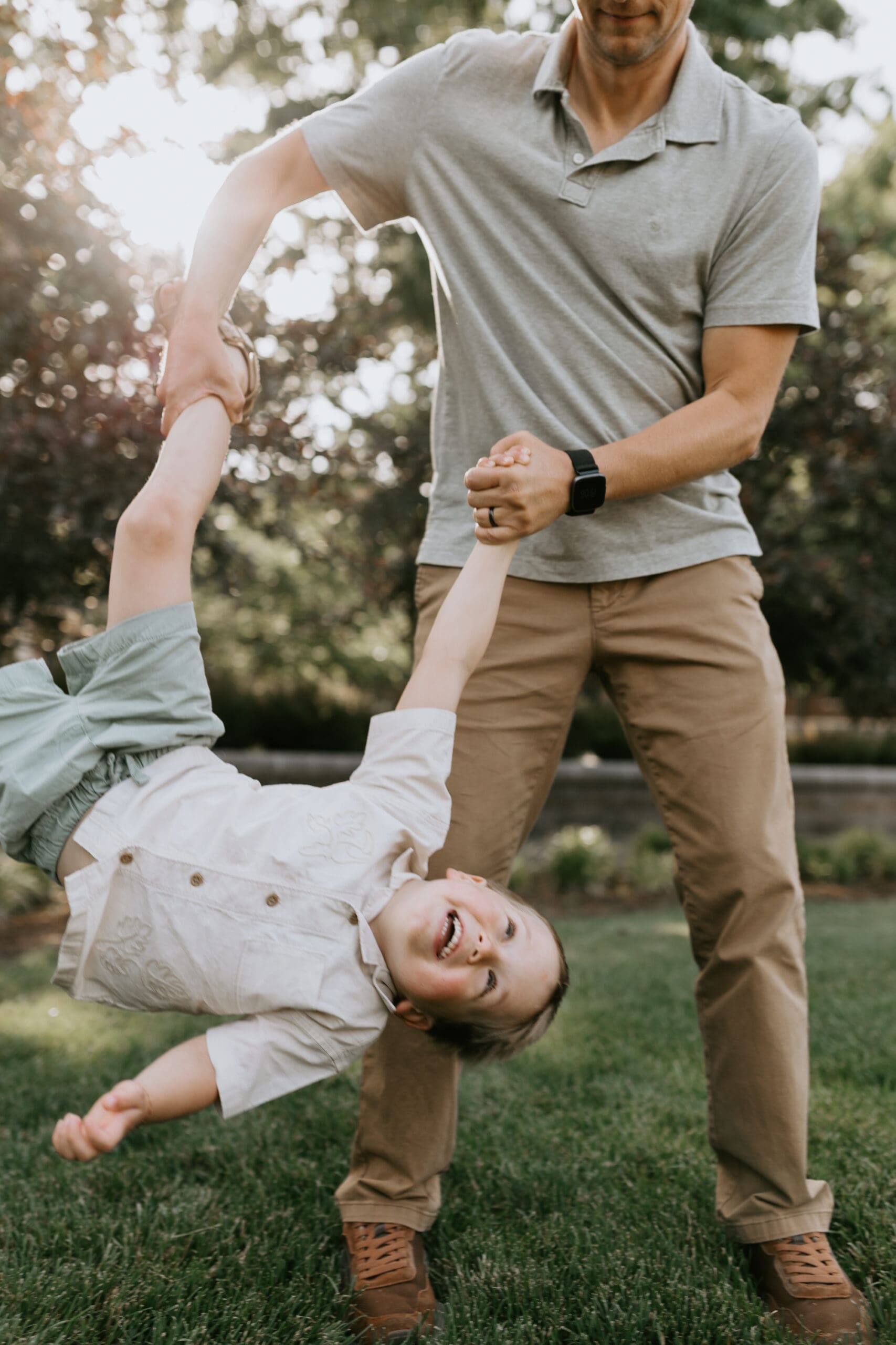 A small child is laughing while being playfully swung by his dad.